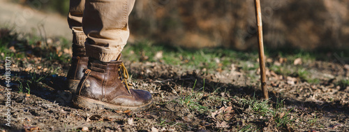 Horizontal banner close-up dirty boots of hiker man walking in a muddy path. Unrecognizable person in outdoors activities.