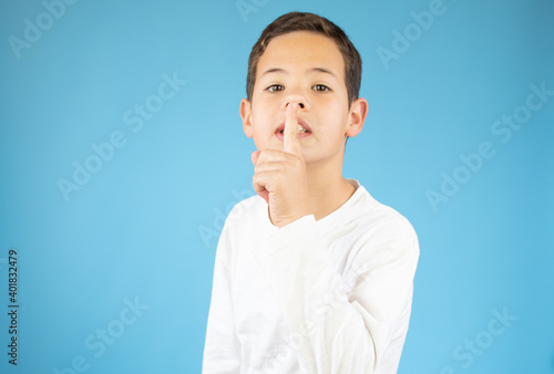 Young caucasian boy is gesturing the silence posing serious on a blue studio wall in casual clothes