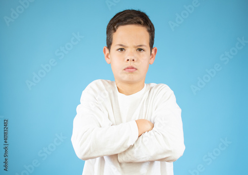 Beautiful caucasian bored boy pouting mouth and thinking with arm crossed gesture isolated blue background