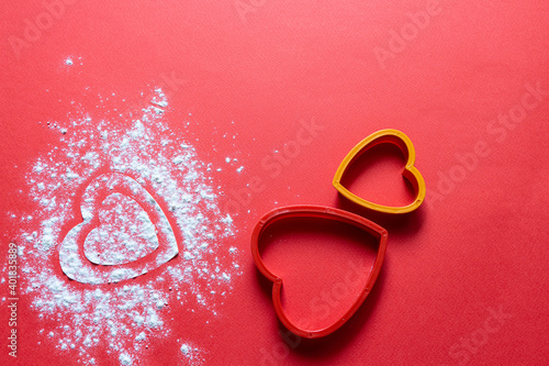 Bakery products. Flour is scattered on the table in the form of hearts. Form for gingerbread. Valentine's day baked goods flour scattered in the shape of a heart on a red background. Christmas 