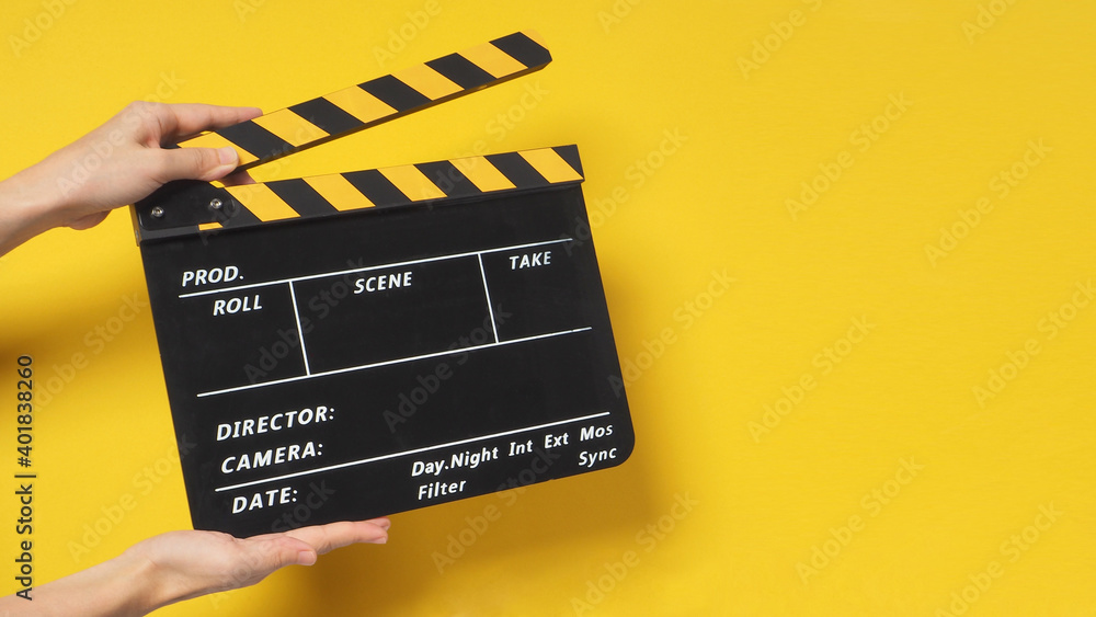 Hand is holding clapper board or movie slate.It is used in film production and cinema,movies industry on yellow background.