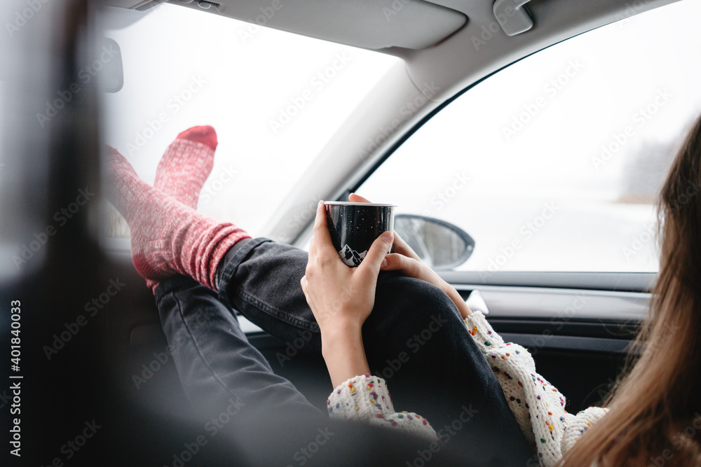 Alone traveler boho woman wearing scarf rest in car and looking away of winter landscape while her journey. Young female sitting in car and get warm with cup of tea Alone traveler boho woman wearing scarf rest in car and looking away of winter landscape while her journey. Young female sitting in car and get warm with cup of tea