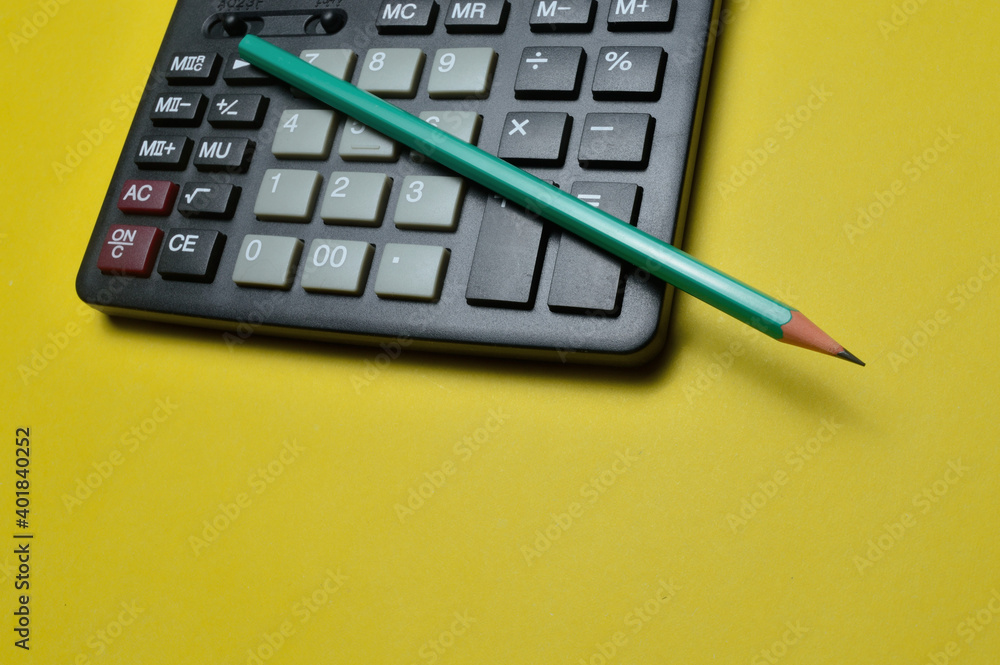 calculator and pencil lie on a yellow background. close-up. calculator and pencil lie on a yellow background. close-up.