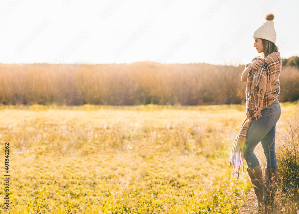 girl in a meadow looking into the distance at sunset.She is pensive dressed in casual clothes and wrapped in a big scarf