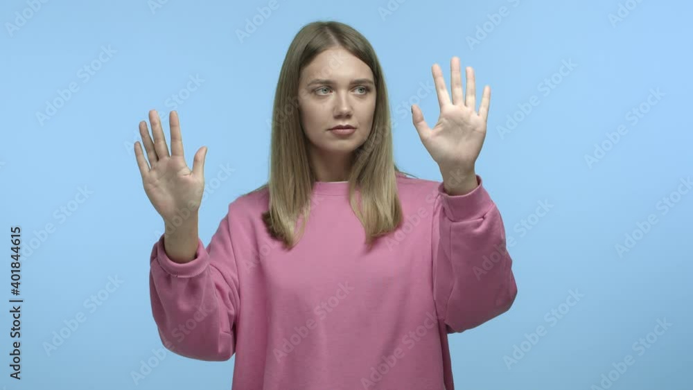 Funny young woman with blond hair touching invisible wall as if being a mime, showing pantomime against blue background Funny young woman with blond hair touching invisible wall as if being a mime, showing pantomime against blue background