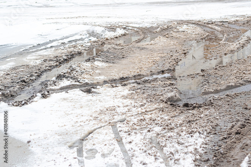 Close-up of a rubble road with potholes, large muddy puddles and melted snow