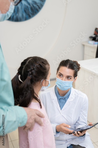 Young female ophthalmologist in protective mask and whitecoat using tablet