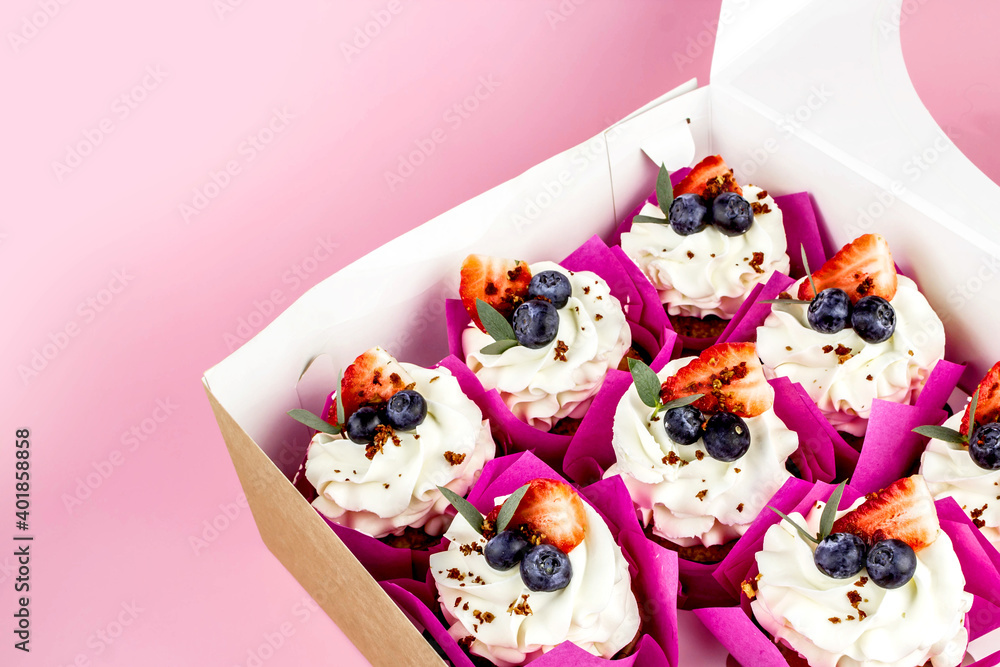 Delicious cupcakes with cream and fresh berries in box on pink background. Copy space. Delicious cupcakes with cream and fresh berries in box on pink background. Copy space.