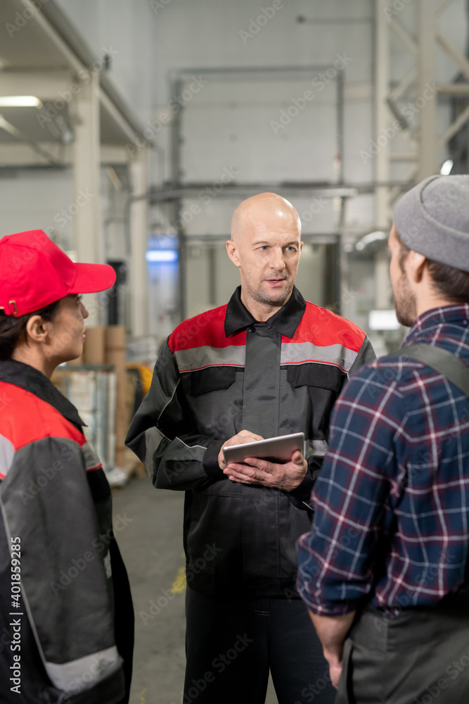 Confident bald mature foreman with tablet having discussion with subordinates Confident bald mature foreman with tablet having discussion with subordinates