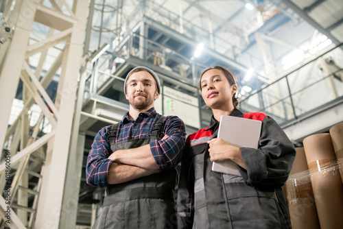 Young successful male and female engineers of large plant looking at you