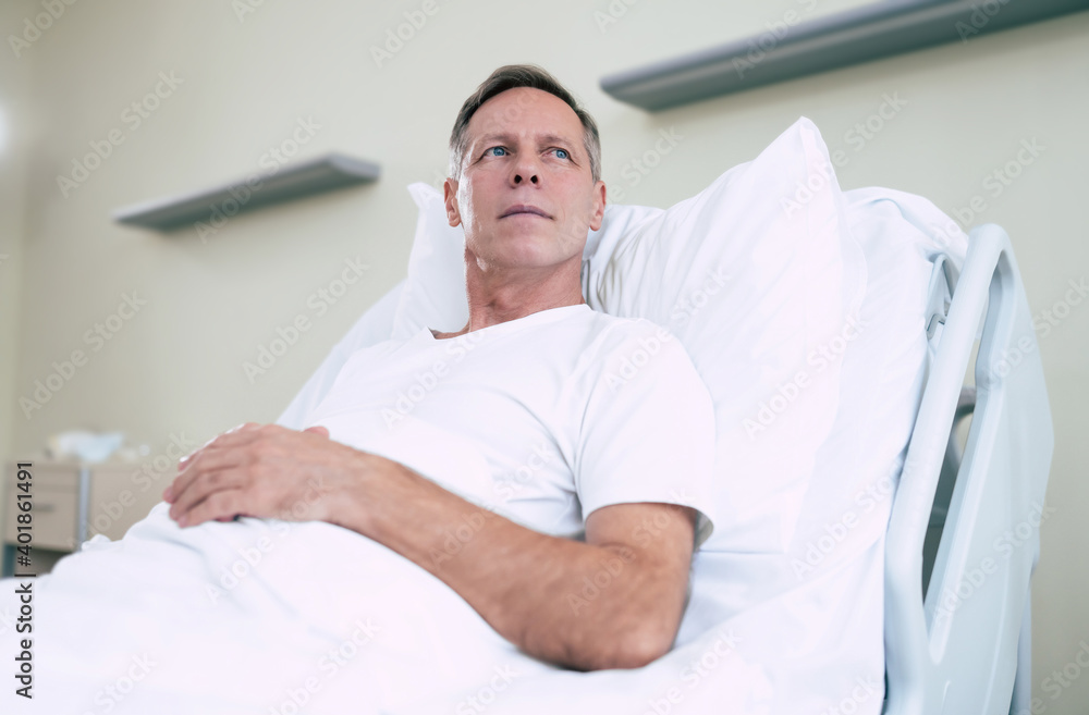 Thoughtful mature patient man is lying on the clinic bed in a hospital ward and looking away Thoughtful mature patient man is lying on the clinic bed in a hospital ward and looking away