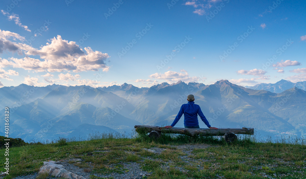 Fototapeta premium person sitting on a bench while admiring the view with mountains