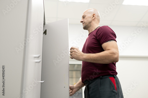 Mature worker of modern factory having drink while opening door of his locker