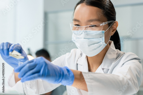Gloved female researcher putting small sample of food ingredient into flask