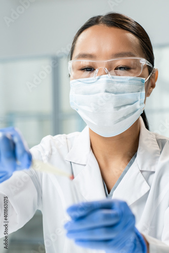 Woman in eyeglasses and mask putting small sample of food ingredient into flask