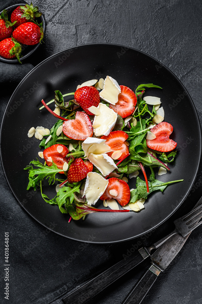 Brie cheese salad with strawberries, nuts, chard and arugula. Black background. Top view