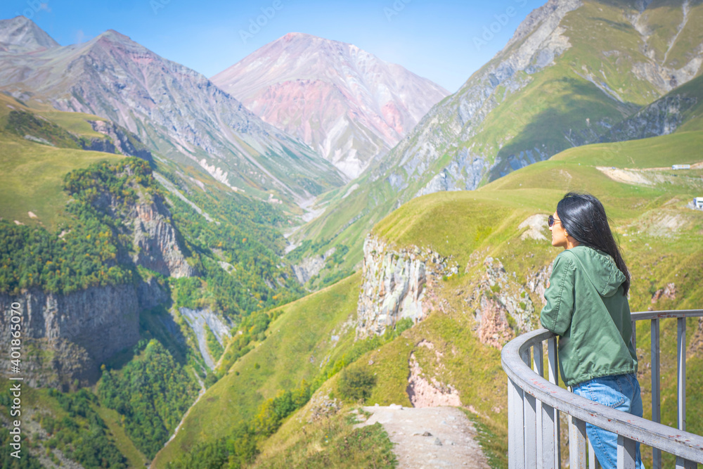 Female woman stands on Gudauri viewpoint platform and looks to scenic mountain landscape of Kazbegi. Travel destination in Georgia