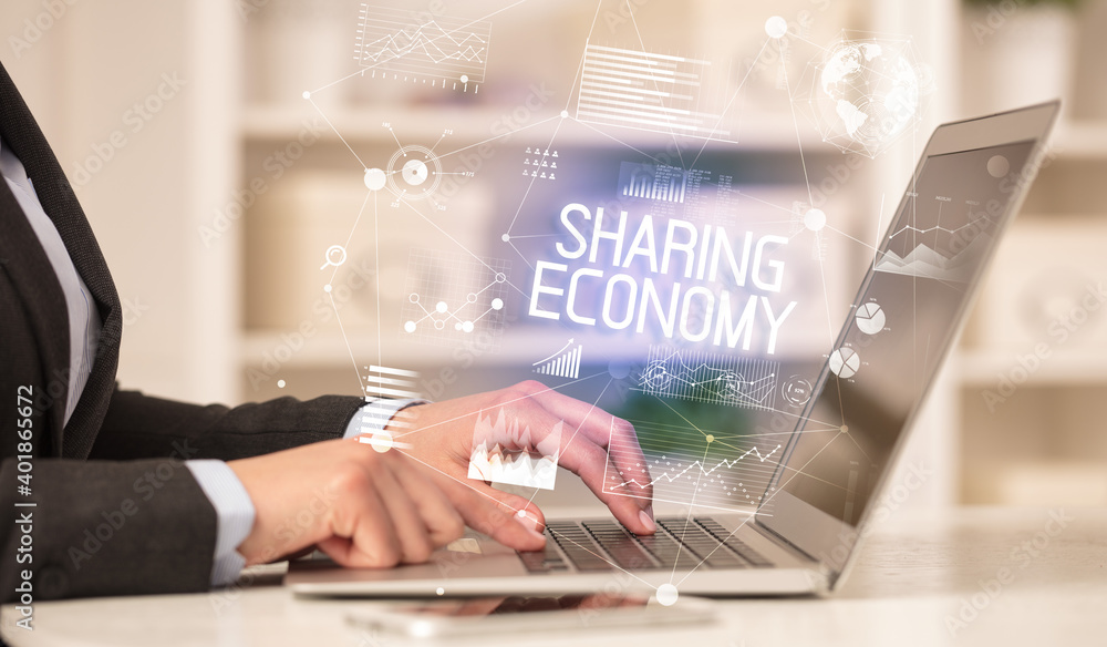 Side view of a business person working on laptop with SHARING ECONOMY inscription, modern business concept Side view of a business person working on laptop with SHARING ECONOMY inscription, modern business concept