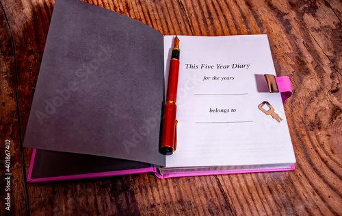 A close up of a five year diary and wooden fountain pen on a wooden background