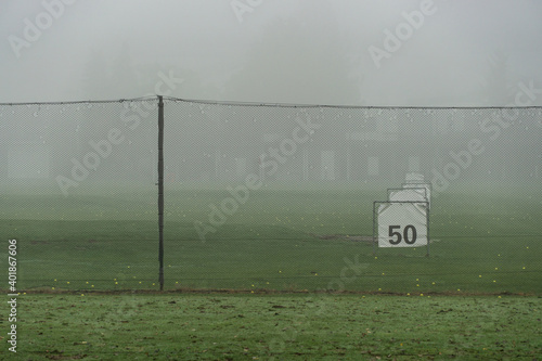Golf driving range in autumn morning fog (behind fence)
