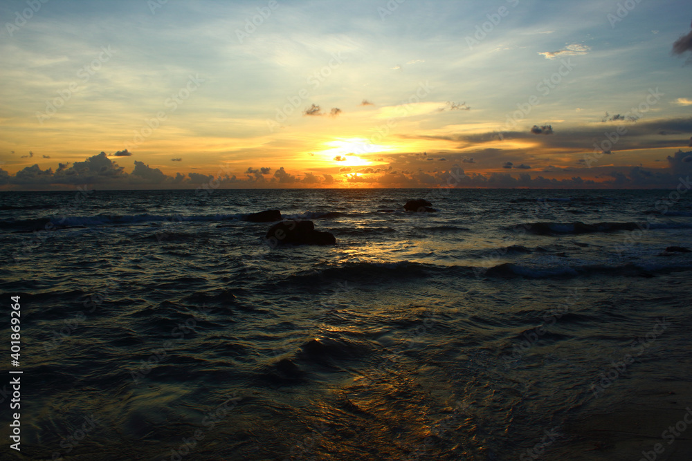 beautiful golden sunset over wavy dark sea with clouds on the blue sky