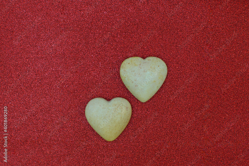 Two polished light stones, carved in the shape of a heart, lie on a beautiful red fabric with sequins. Valentine's Day and love symbol. Flat lay. Copy space, holiday card Two polished light stones, carved in the shape of a heart, lie on a beautiful red fabric with sequins. Valentine's Day and love symbol. Flat lay. Copy space, holiday card