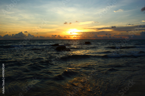 beautiful golden sunset over wavy dark sea with clouds on the blue sky © M.i.c.c.a