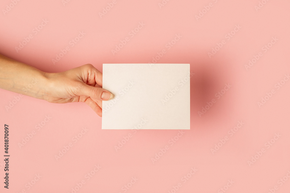 Female hand holding a card on a pastel pink background. Flat lay, top view Female hand holding a card on a pastel pink background. Flat lay, top view