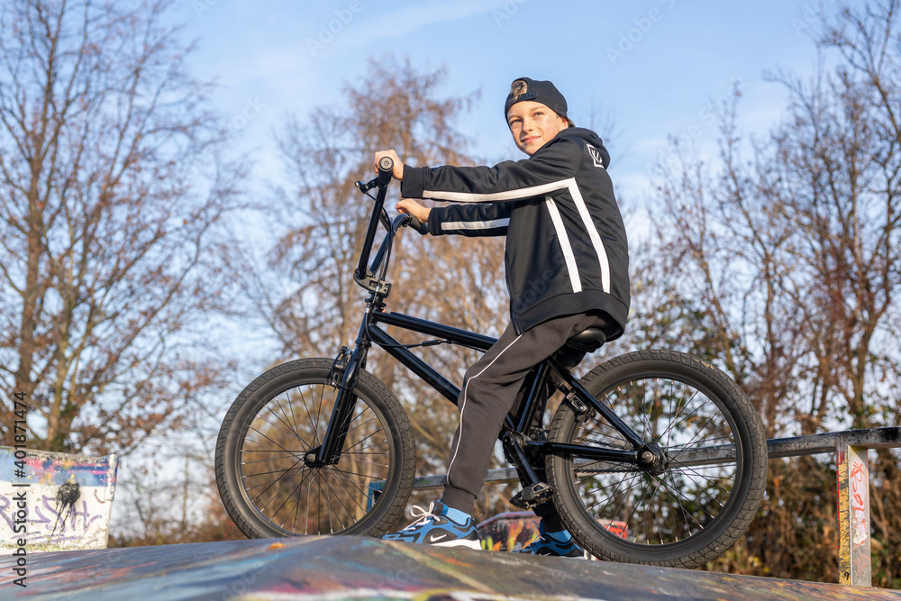 Junge mit schwarzen BMX-Fahrrad auf einem Sportplatz/Bahn. BMX-Räder sind das kleine Bike für große Sprünge. Beliebt als Sportgerät, mit dem künstliche Hindernisse und Kurven gemeistert werden.