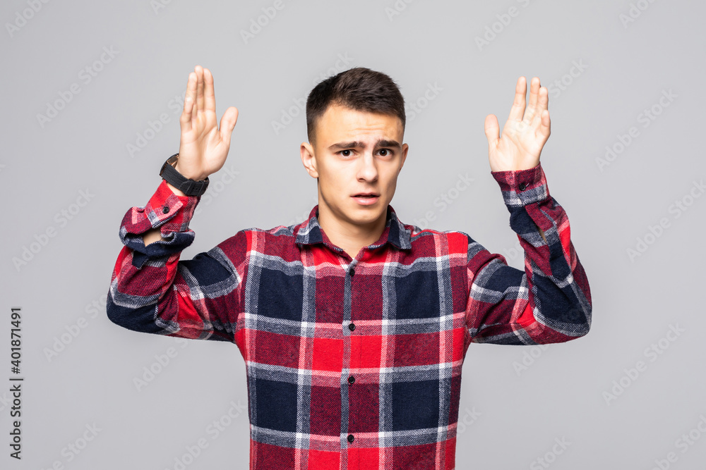 Naklejka premium Portrait of young handsome man with raised hands against grey background