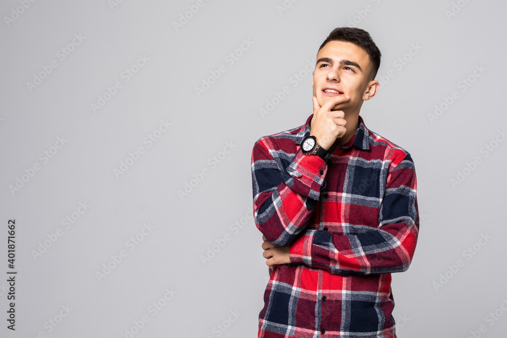 Handsome young man standing and lhands on chin isolated on the gray background Handsome young man standing and lhands on chin isolated on the gray background