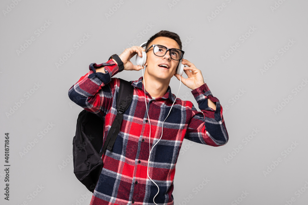 Young man with a backpack in headphones isolated on a gray background. Student with a bag listens to music. Young man with a backpack in headphones isolated on a gray background. Student with a bag listens to music.