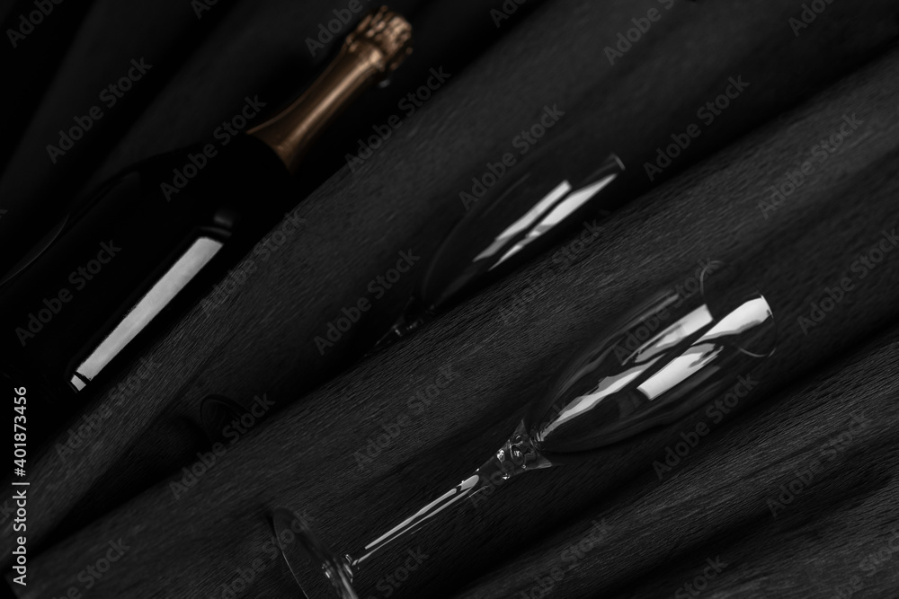 Naklejka premium Two champagne glasses and bottle on black background. Celebrating New Year, Valentine day.