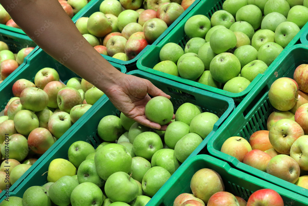 young male hand holding a green apple over a bunch of apples at the supermarket