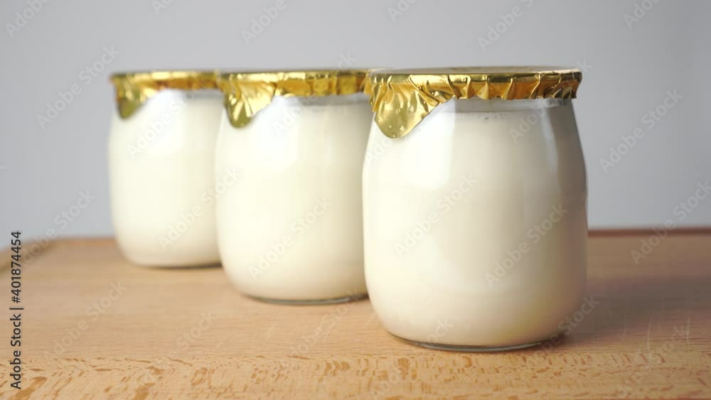 Natural yoghurt in glass jars with golden foil lids. Close up. Wooden cutting board Natural yoghurt in glass jars with golden foil lids. Close up. Wooden cutting board