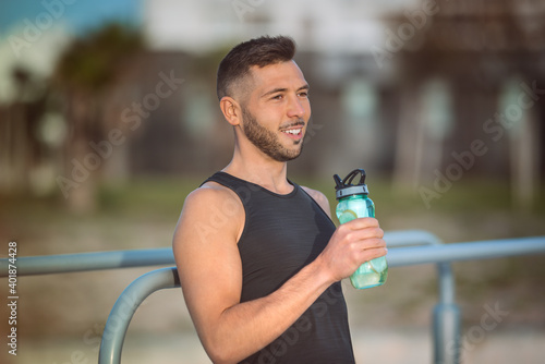 Young fitness man drinking water with lemon from reusable bottle during a workout. Drinking while exercising. Dehydration while training