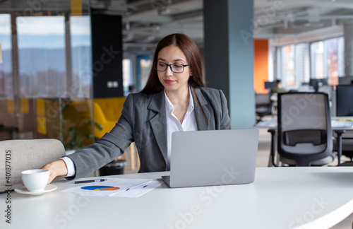 A young businesswoman with glasses in the office is working on a laptop. 