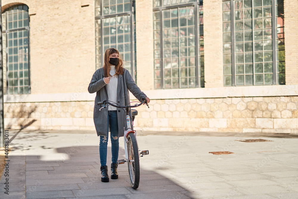 Pretty Caucasian Young Girl Rides a Bicycle in the City, Wearing a Black Mask