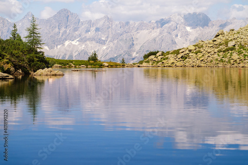 Fototapeta Naklejka Na Ścianę i Meble -  Magical idyllic landscape with lake in mountains in Alps Europe. tourist trail on green hills in Alps. Beautiful rock and admire amazing view to mountain peaks. Fantastic sunny day is in mountain lake