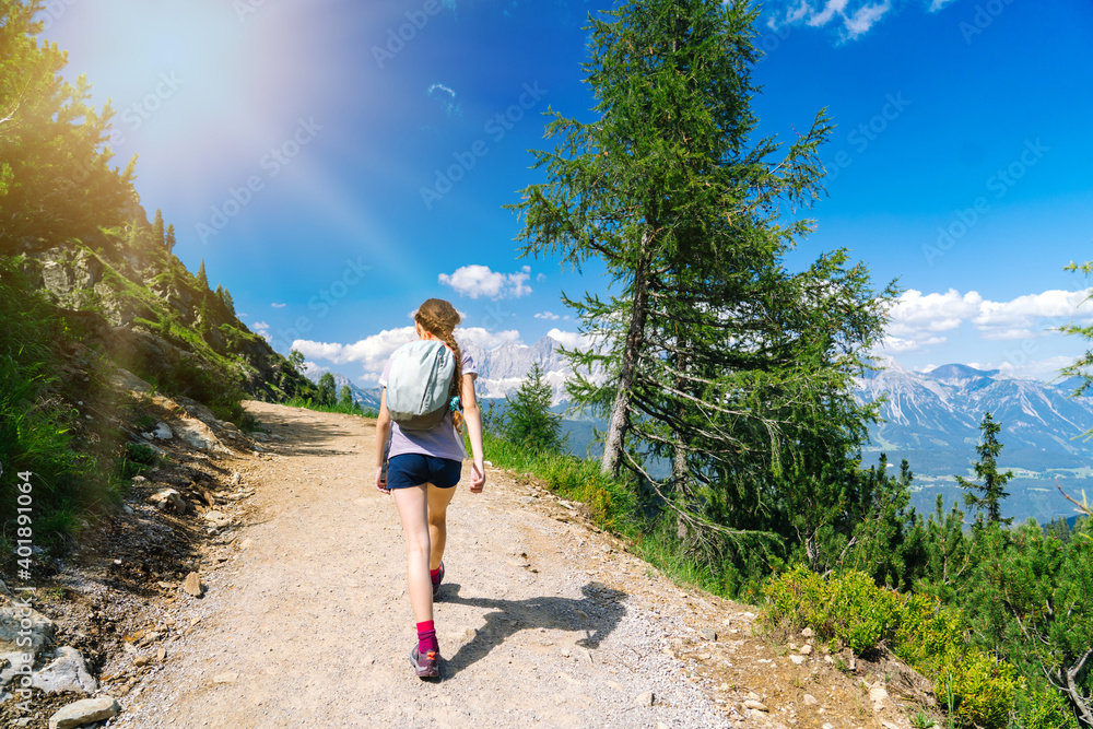 Girl hiking on beautiful summer day in alps mountains Austria, resting on rock and admire amazing view to mountain peaks. Active family vacation leisure with kids. Outdoor fun and healthy activity