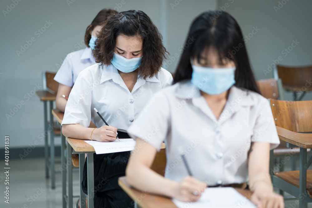 Cheerful college students in the classroom wear protective face masks and use antiseptic for coronavirus prevention during coronavirus pandemic. Group of students wearing protection masks in class.