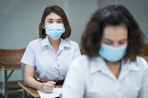 Cheerful college students in the classroom wear protective face masks and use antiseptic for coronavirus prevention during coronavirus pandemic. Group of students wearing protection masks in class.