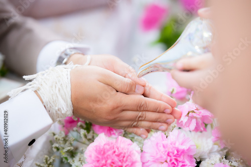 Water pouring in to bless the bride and groom in a Thai wedding ceremony. The groom's hands are resting and placed on the pillow to receive the blessing of relatives or friends. photo