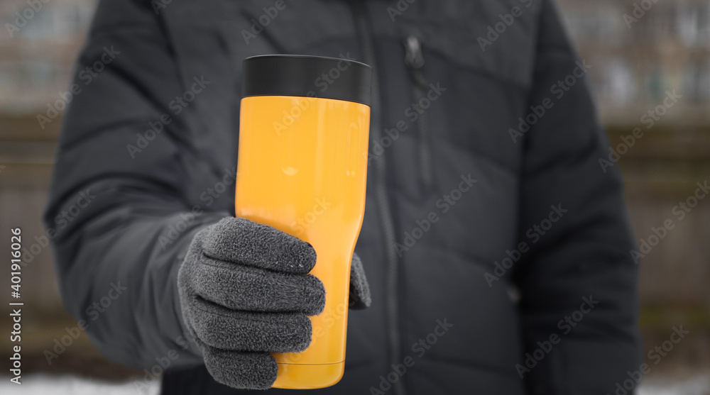 A man in winter clothes holds a thermos of hot drinks. Walking outdoors in winter with the cold. A man in winter clothes holds a thermos of hot drinks. Walking outdoors in winter with the cold.