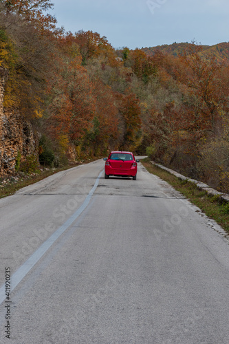 view of a red car driving in the streeets among the forest 4 with fall colours near in zagori epirus greece