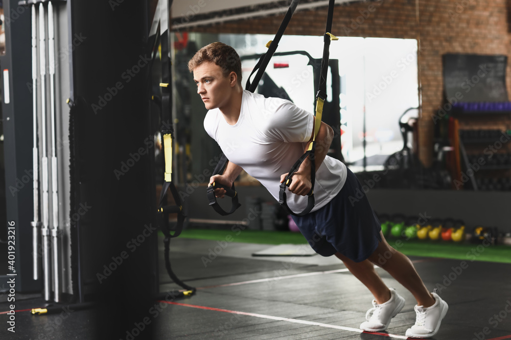 Handsome muscular man exercising with TRX straps in gym Handsome muscular man exercising with TRX straps in gym