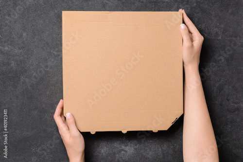 Hands with cardboard pizza box on dark background