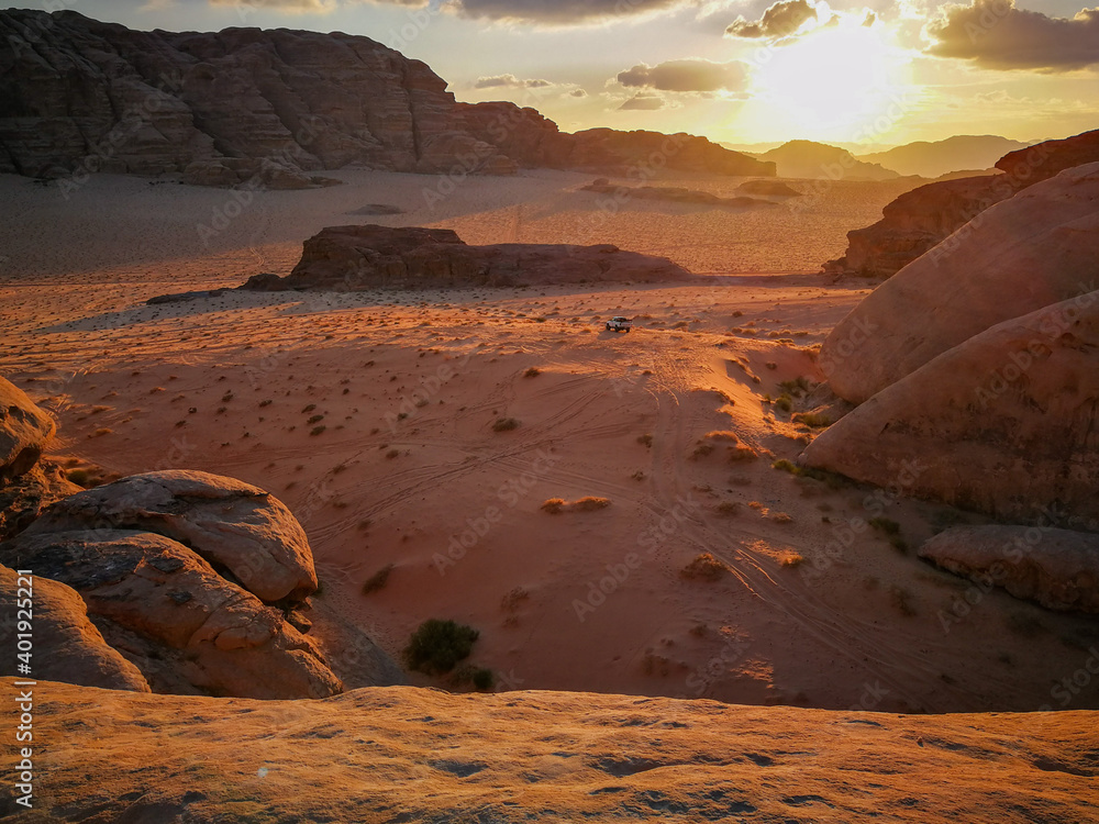 Fototapeta premium Wadi Ram desert valley surrounded by mountains, car rides in the valley, evening sun illuminates the landscape, nature of Jordan
