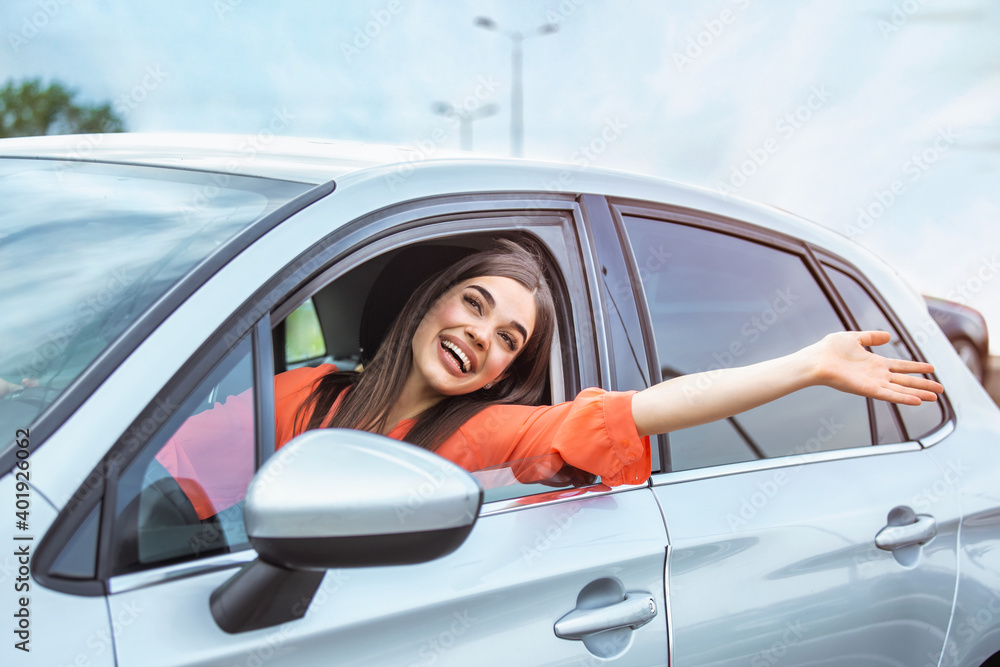 Young woman sitting in a car hand out of window. Happy woman driving a car and smiling. Portrait of happy female driver steering car with safety belt. Cute young lady happy driving car.