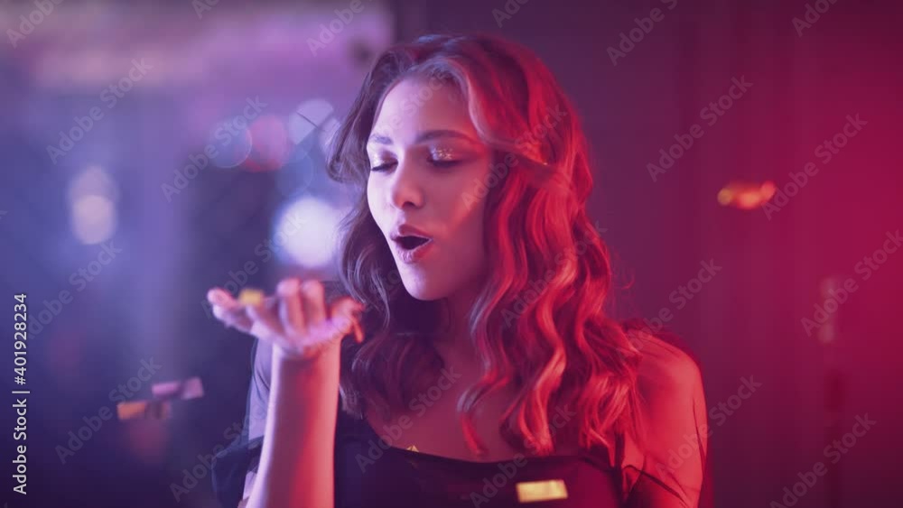 Portrait of glamour female in the luxury party, young female blows up confetti and smiling, golden confetti flying in the air, neon light, 4k slow motion. Portrait of glamour female in the luxury party, young female blows up confetti and smiling, golden confetti flying in the air, neon light, 4k slow motion.